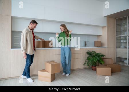 Die Frau freut sich über den Umzug und springt vor Freude, als der zufriedene Ehemann die letzten Kisten der Zugehörigkeit einbringt Stockfoto