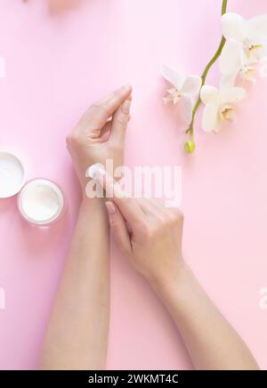 Werbung für kosmetische Creme. Handcreme, eine Frau schmiert ihre Hände mit Creme auf dem Hintergrund weißer Orchideen. Stockfoto