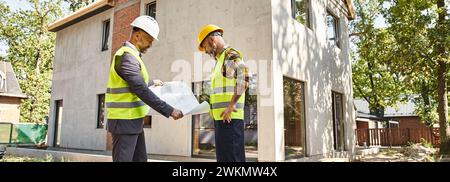 Engagierter Hüttenbauer und Architekt, der einen Plan hält und über Baustelle, Banner diskutiert Stockfoto