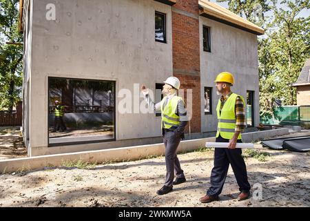 Engagierter Architekt und Baumeister in Sicherheitswesten mit Bauplänen und Besprechung des Bauprozesses Stockfoto