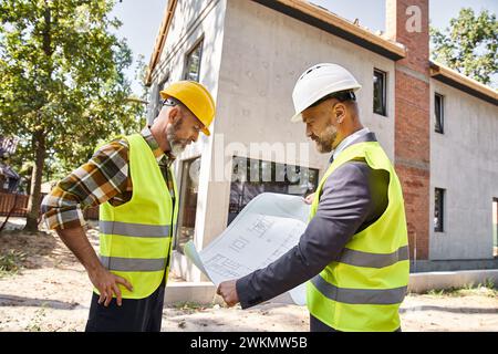 Engagierter Hüttenbauer und Architekt, der Pläne hält und Baustelle diskutiert Stockfoto