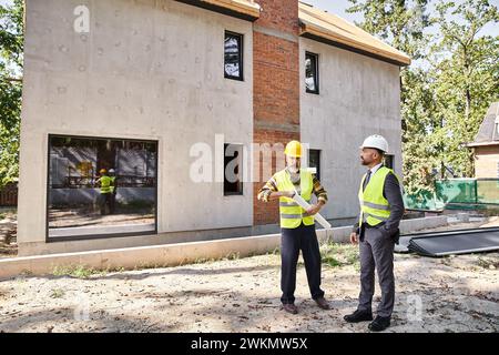 Engagierter Architekt und Baumeister in Sicherheitswesten mit Bauplänen und Besprechung des Bauprozesses Stockfoto