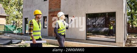 Engagierter Architekt und Baumeister in Sicherheitswesten mit einem Entwurf, der den Bauprozess erläutert, Banner Stockfoto