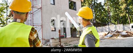 Rückansicht von Hüttenbauern in Schutzhelmen mit einem Entwurf, der ihre Arbeit vor Ort bespricht, Banner Stockfoto