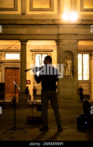 Busking in Italien ist eine altehrwürdige Tradition, bei der Musiker auf den Straßen spielen, um Trinkgeld zu erhalten. Ein Mann spielt nachts in der Nähe der Uffizien Geige. Stockfoto