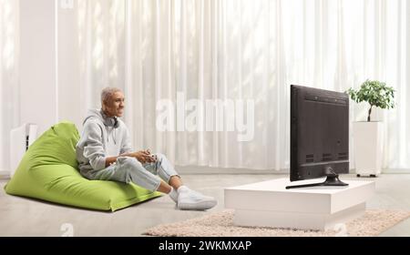 afroamerikaner sitzt auf einem grünen Sitzsack und spielt ein Videospiel mit Joystick Stockfoto