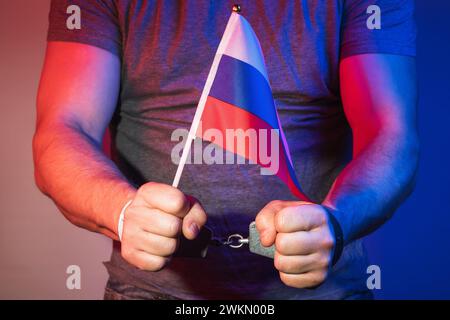 Hände eines Mannes in Handschellen, der eine russische Flagge hält, Konzept zum Thema Spionage Stockfoto