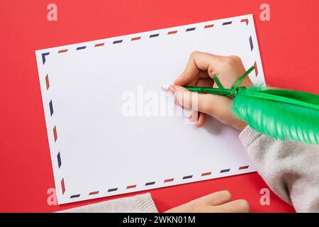 Kinderhand mit federförmigem Stift auf einem Glückwunschumschlag, Vorlage für den Designer Stockfoto