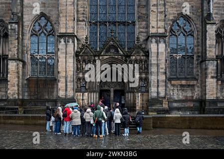 Touristen auf einem Spaziergang durch Edinburghs Altstadt, die an einem nassen Frühlingsmorgen vor der St. Giles Kathedrale stehen. Stockfoto