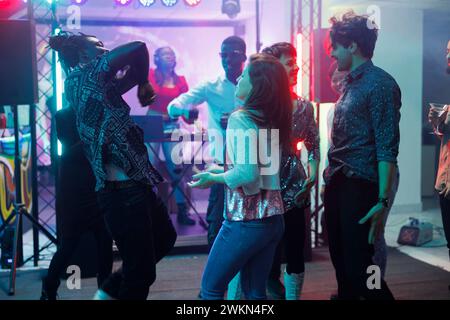 Freunde tanzen bei einem Konzert im Nachtclub, haben Spaß und bewegen sich auf der Tanzfläche. Leute, die feiern und dj-Live-Musik auf der Bühne genießen, während sie die Diskothek im Club besuchen Stockfoto