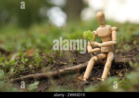 Hölzerne Menschenfigur mit jungen grünen Sämlingen auf dem Boden draußen, Platz für Text Stockfoto