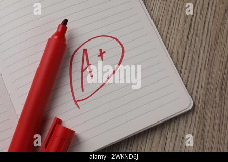 Schulklasse. Roter Buchstabe A mit Pluszeichen auf Notizbuchpapier und Markierer auf Holztisch, Draufsicht Stockfoto