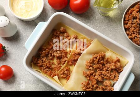 Lasagne kochen. Pasta-Blätter, Hackfleisch in Backblech und Produkte auf einem hellen, strukturierten Tisch, flach liegend Stockfoto