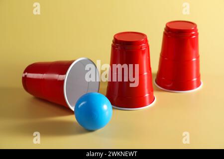 Shell-Spiel. Drei rote Becher und Ball auf gelbem Hintergrund Stockfoto