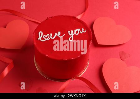 Bento Kuchen mit Text Love You, Band und Papierherzen auf rotem Tisch. St. Valentinstag-Überraschung Stockfoto