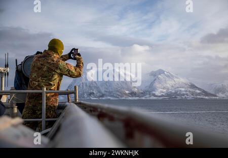 Harstad, Norwegen. Februar 2024. Ein italienischer Seemann fotografiert die Berge, als das Dock-Landungsschiff USS Gunston Hall (LSD 44) der Whidbey-Island-Klasse in Harstad, Norwegen, ankommt, um am 24. Februar 2024 den standhaften Defender zu unterstützen. Der standhafte Verteidiger 2024, die größte Übung der NATO seit Jahrzehnten, wird zeigen, dass die NATO in der Lage ist, schnell Truppen aus der gesamten Allianz zu entsenden, um die Verteidigung Europas zu stärken. (Kreditbild: © Danielle Serocki/U.S. Navy/ZUMA Press Wire) NUR FÜR REDAKTIONELLE ZWECKE! Nicht für kommerzielle ZWECKE! Stockfoto