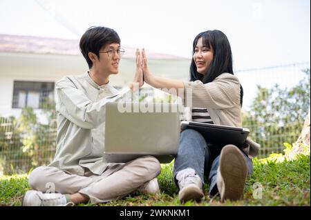 Zwei fröhliche asiatische Universitätsstudenten geben sich gegenseitig fünf, feiern ihren Projekterfolg oder testen gemeinsam auf t Stockfoto