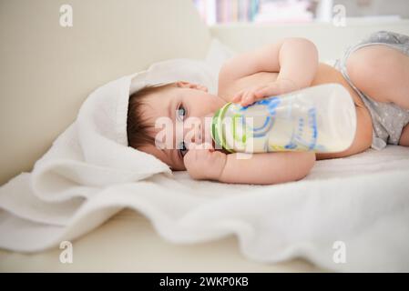 Baby, Flasche und Entspannung mit dem Jungen, Ruhe und Ernährung mit Wellness und Kinderbetreuung mit Decke. Haus, Kind und Neugeborenes trinken Milch mit Wachstum und Stockfoto