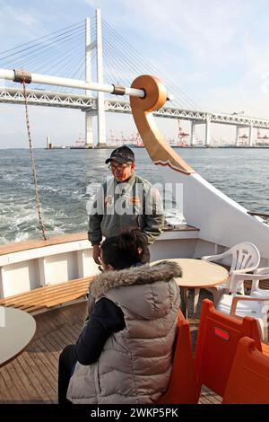 Ein Kreuzfahrtschiff in der Yokohama Bay mit Yokohama Gate Bridge im Hintergrund und einem Passagier im Boot. Stockfoto