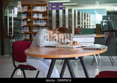 Müde Studentin, die auf dem Schreibtisch in der Bibliothek schläft. Stockfoto