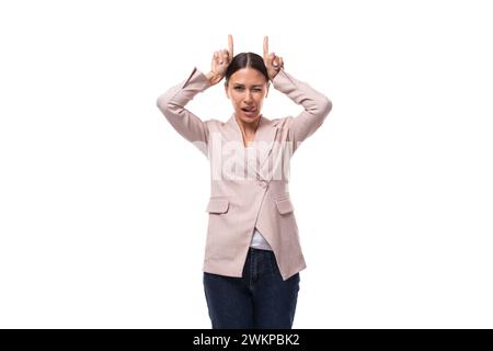 Hübsche schlanke junge Frau mit schwarzem Haar in einer Jacke macht eine Grimasse auf weißem Hintergrund mit Kopierraum Stockfoto