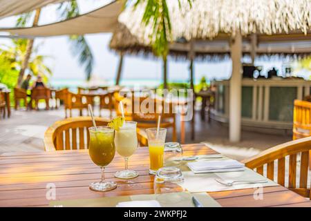 Tropisches Restaurant im Freien mit Holztischen, Stühlen unter Palmen und Cocktails im luxuriösen Strandresort. Cocktails für Sommerreisen aus der Nähe Stockfoto