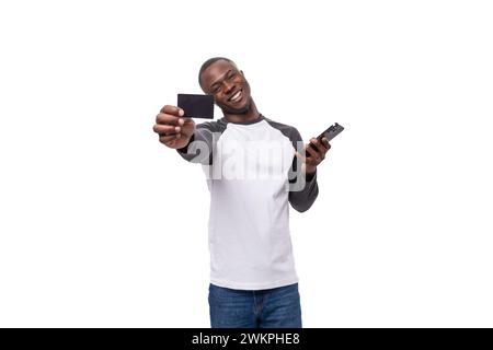 Ein junger gutaussehender afrikaner, der in einem Sweatshirt gekleidet ist, hält ein Plastikkartenmockup Stockfoto