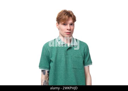 Ein junger, schlanker Ingwermann mit einem Tattoo auf dem Arm, gekleidet in einem grünen T-Shirt mit hellen Gesichtsausdrücken Stockfoto