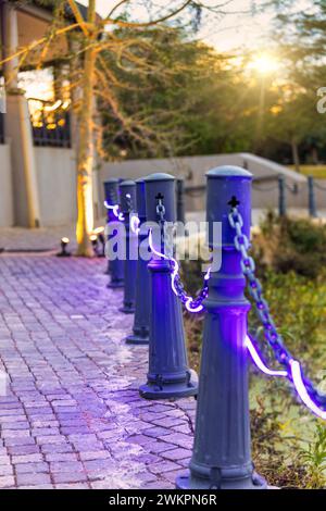 Gepflasterte Gasse mit violettem Licht, das an den Metallsäulen gehängt ist Stockfoto