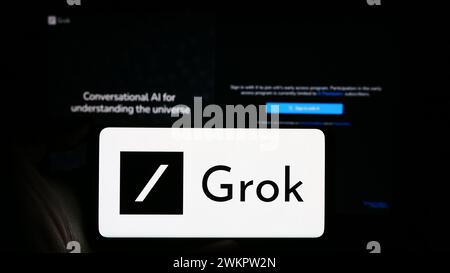 Person, die ein Mobiltelefon mit dem Logo des Chatbots Grok (X.AI) für generative künstliche Intelligenz vor der Webseite hält. Schwerpunkt auf dem Display des Telefons. Stockfoto
