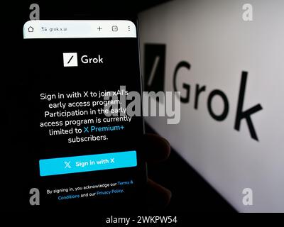 Person, die ein Handy hält, mit Webseite des generativen Chatbots Grok (X.AI) mit Logo. Konzentrieren Sie sich auf die Mitte des Telefondisplays. Stockfoto