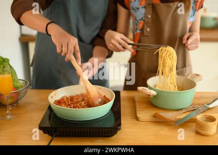 Ein Foto von einem glücklichen jungen Paar, das Schürzen trägt, die köstliche Bolognese-Sauce zum Abendessen in der Küche machen Stockfoto