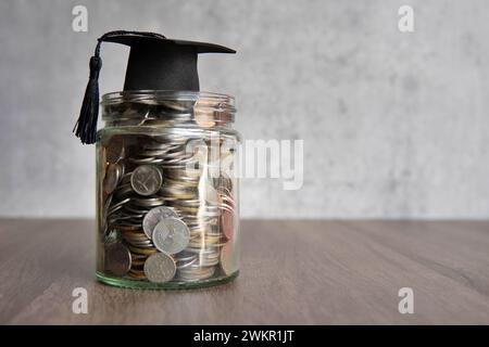 Glasgefäß gefüllt mit Münzen und einer Graduierungskappe darauf. Kopierbereich für Text. Einsparungskonzept im Bildungsbereich. Stockfoto