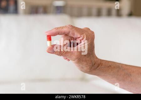 Nahaufnahme einer alten weiblichen Hand, die eine rot-weiße Kapselpille in zwei Fingern hält. Gesundheitsvorsorge-Frauenkonzept Stockfoto