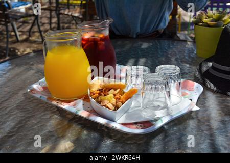 Kalte Sangria und kalter Orangensaft in Glaskaraffen, Gläser und Nüsse auf einem Tisch, serviert auf einer Terrasse an einem heißen Sommertag Stockfoto