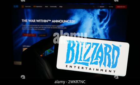 Person mit Smartphone und Logo des US-amerikanischen Videospielunternehmens Blizzard Entertainment Inc. Vor der Website. Schwerpunkt auf dem Display des Telefons. Stockfoto