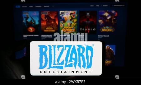Person, die ein Mobiltelefon mit dem Logo des US-amerikanischen Videospielunternehmens Blizzard Entertainment Inc. Vor der Webseite des Unternehmens hält. Schwerpunkt auf dem Display des Telefons. Stockfoto