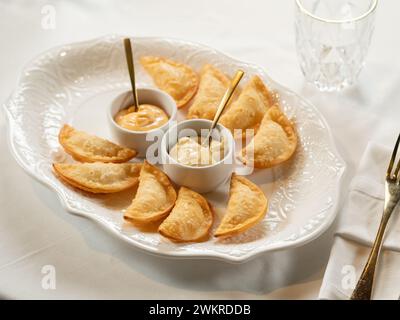 Heiße Vorspeisen mit Mini Chebureki und Saucen isoliert auf weißem Tischhintergrund. Restaurant-Vorspeisenmenü mit knusprigen gebrannten Vorspeisen, Pies oder Samosa mit scharfer Sause aus nächster Nähe Stockfoto