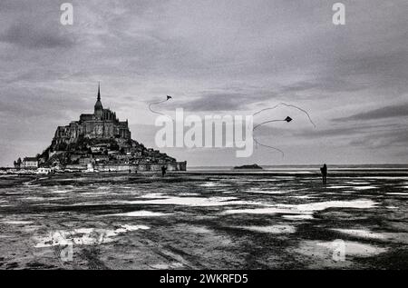 Mont-Saint-Michel, Normandie, Frankreich 1988 Flying Kites am Sandstrand mit Mont-Saint-Michel als Kulisse. Mont-Saint-Michel Norman: Mont Saint Miché; englisch: Saint Michael's Mount) ist eine Gezeiteninsel und Festlandgemeinde in der Normandie. Die Insel liegt etwa einen Kilometer vor Frankreichs Nordwestküste, an der Mündung des Flusses Couesnon bei Avranches und ist 7 Hektar groß. Der Festlandteil der Gemeinde hat eine Fläche von 393 Hektar (971 Acres), so dass die Gesamtfläche der Gemeinde 400 Hektar (990 Acres) beträgt. Die Lage der Gemeinde – auf einer Insel nur wenige Stockfoto