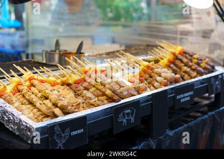 Eine appetitliche Auswahl an gegrillten Spießen mit Hühnchen, Schweinefleisch und mit Speck gewickelten Würstchen, begleitet von Gemüse, wird in einem Street Food stan präsentiert Stockfoto