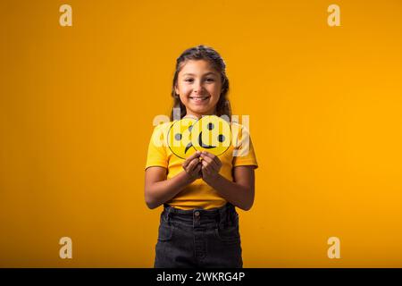 Porträt eines lächelnden Mädchens, das traurige und glückliche Emoticons in der Hand hält. Psychische Gesundheit, Psychologie und kindliches Gefühlskonzept Stockfoto