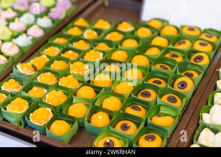 Eine Auswahl an bunten thailändischen Desserts, darunter Thong Ek und Khanom Ja Mong Got, präsentiert in umweltfreundlichen Bananenblattbechern auf einem Straßenmarkt Stockfoto