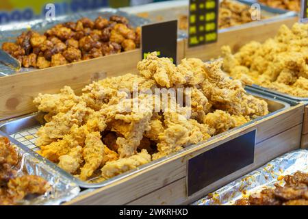 Tabletts gefüllt mit knusprigen, goldfrittierten Hähnchenstücken, die auf einem geschäftigen Lebensmittelmarkt serviert werden können Stockfoto