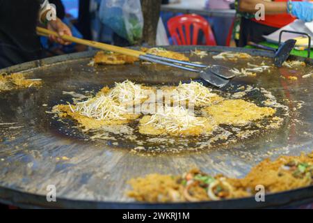 Der thailändische Street Food Koch bereitet ein traditionelles knuspriges Austernomelett zu, garniert mit frischen Bohnensprossen auf einem großen eisernen Grill Stockfoto