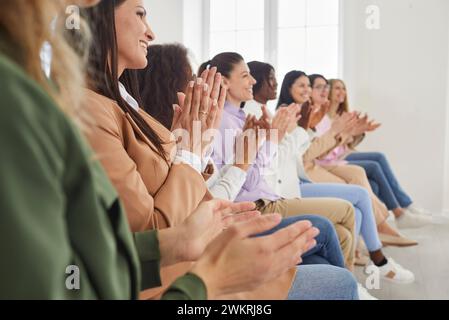 Lächelnde, glückliche Gruppe von Geschäftsfrauen, die in einer Reihe beim Treffen sitzen und applaudieren. Stockfoto