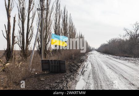 DONETSK REG., UKRAINE - 14. Februar 2024: Krieg in der Ukraine. Eine zerrissene, aber stolz fahrende Flagge ist entlang einer Straße in der Region Donezk zu sehen, ein Symbol für eine unbesiegbare freie Ukraine. Stockfoto