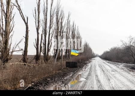 DONETSK REG., UKRAINE - 14. Februar 2024: Krieg in der Ukraine. Eine zerrissene, aber stolz fahrende Flagge ist entlang einer Straße in der Region Donezk zu sehen, ein Symbol für eine unbesiegbare freie Ukraine. Stockfoto