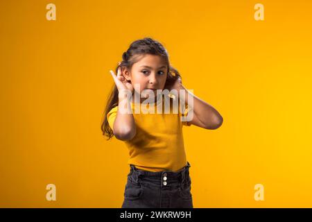 Porträt eines kleinen Mädchens, das lauscht, vertrauliche geheime Gespräche hört, die Hand am Ohr hält. Privatheit- und Neugier-Konzept Stockfoto