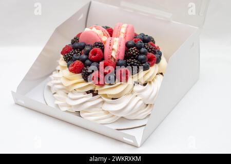 Wunderschöner Kuchen mit Schlagsahne, Makronen und frischen Beeren in einer Geschenkbox auf neutralem Hintergrund Stockfoto