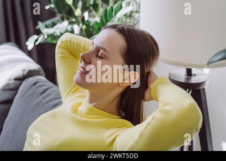 Nahaufnahme einer ruhigen jungen Frau, die sich ausruhen, frische Luft atmen und geistiges Gleichgewicht spüren, Wohlbefinden zu Hause auf der Couch genießen, zufriedenes Mädchen, das Freude daran hat Stockfoto